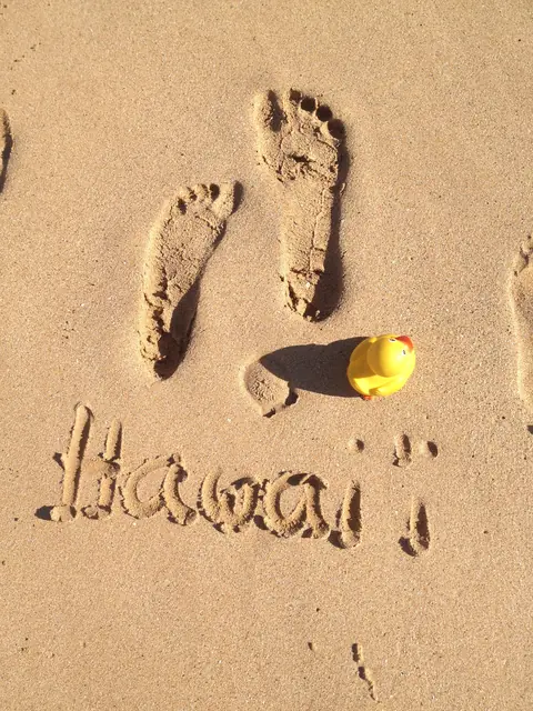 Füße und Ducky im Sand, „Hawai'i“ geschrieben
